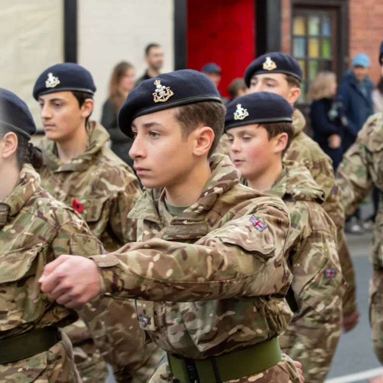 Soldiers in camouflage uniforms marching, wearing navy berets with a crest emblem.
