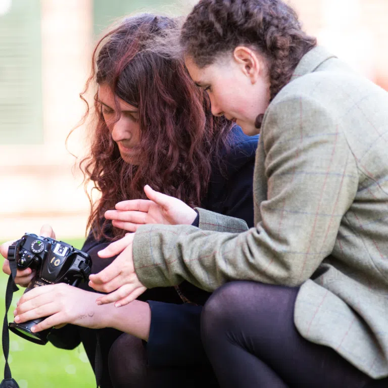 Two people embracing closely outdoors, with a camera visible in the foreground on the left.