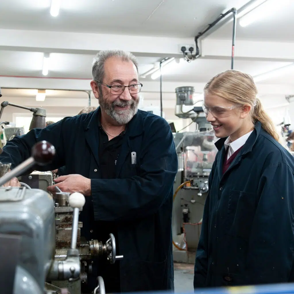 Two coworkers in a workshop inspecting a machine together, wearing protective clothing and safety gear.