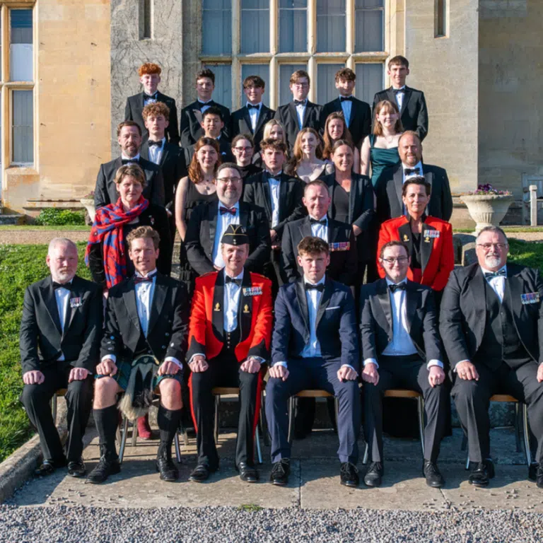 Group of students and adults in formal attire posing on stone steps outside a beige building for a class photo.