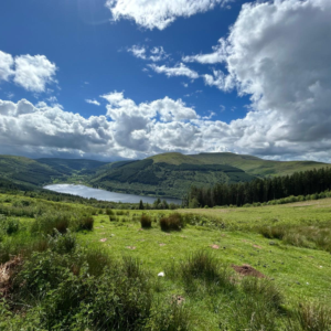 Wide valley with green hills, a winding river, and a blue sky with fluffy clouds.