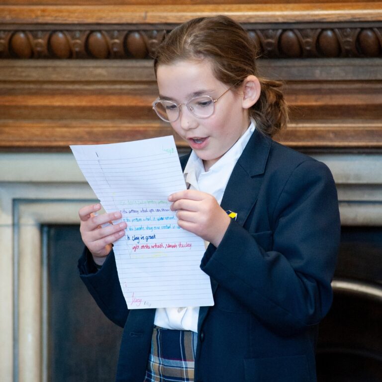 Girl in school uniform reading a handwritten letter with colorful highlights, standing by a wood-paneled wall.