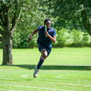 Male athlete in a blue uniform sprinting on a grassy field, holding a green baton in a relay race.