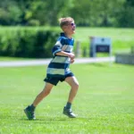 A child running on a sunny grassy field, wearing a blue and white striped shirt and sunglasses, smiling as they move.
