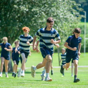 Group of young men running on a sunny grassy field, wearing blue and white striped jerseys during a race.