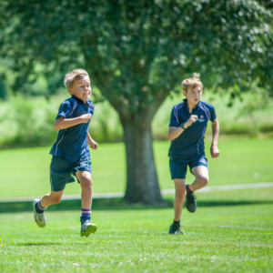 Two young boys running on a sunny grassy field in blue athletic shirts.