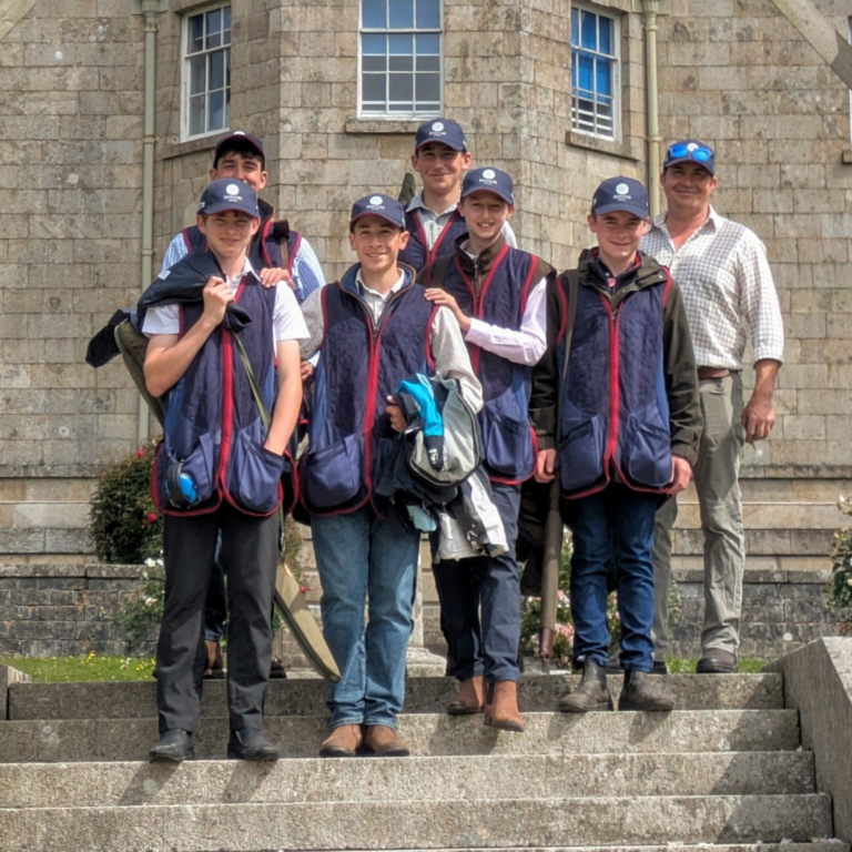 Group of young people in matching navy vests and caps posing on stone steps outside a brick building.
